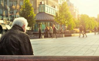 Rear view of older man sitting on a bench in a city