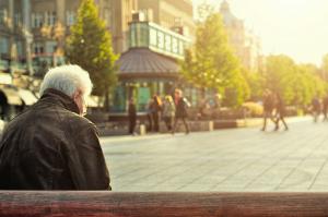 Rear view of older man sitting on a bench in a city